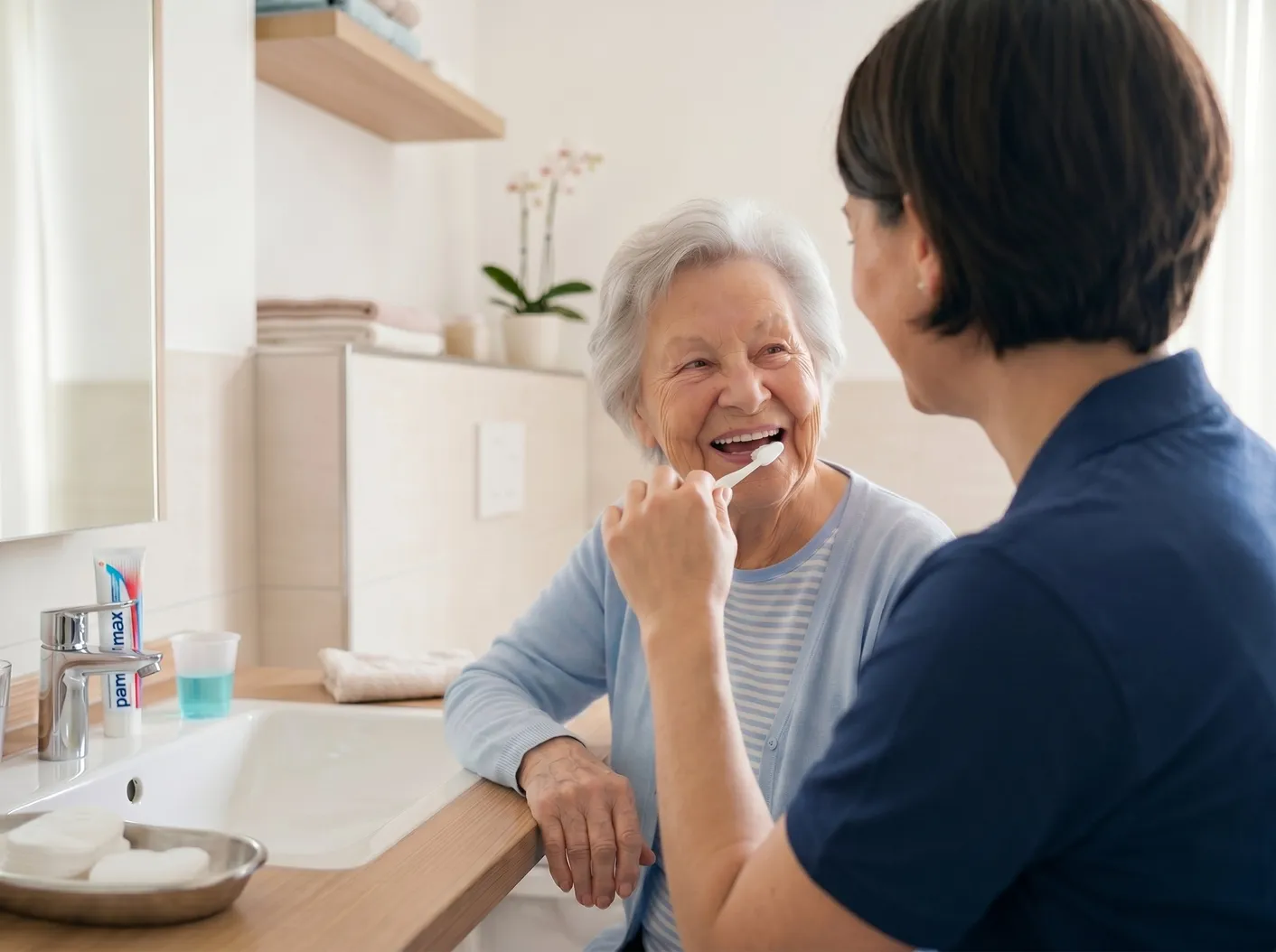Zahnärztin begleitet eine Seniorin beim Zähneputzen im Bad einer Pflegeeinrichtung