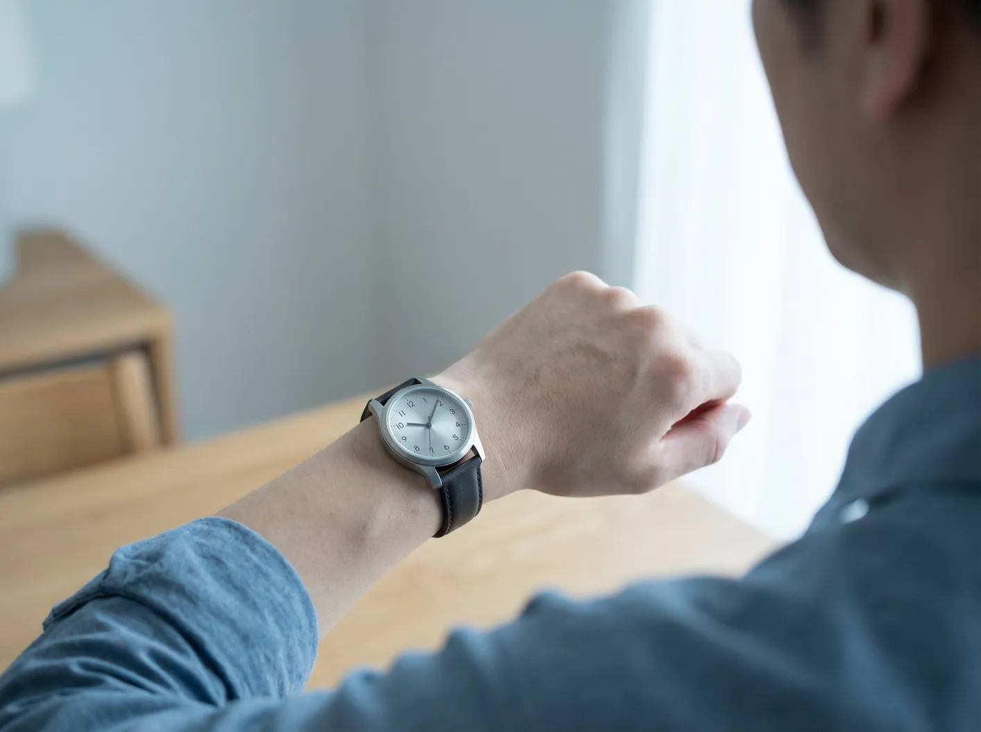 Person sitzt an einem Holztisch und schaut auf die Armbanduhr an ihrem Handgelenk